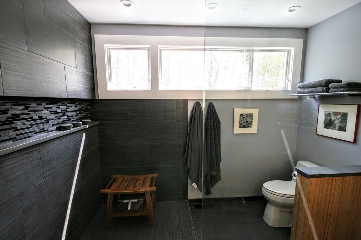 Modern bathroom with dark tiles and a wooden stool in a remodeled home in Mashpee