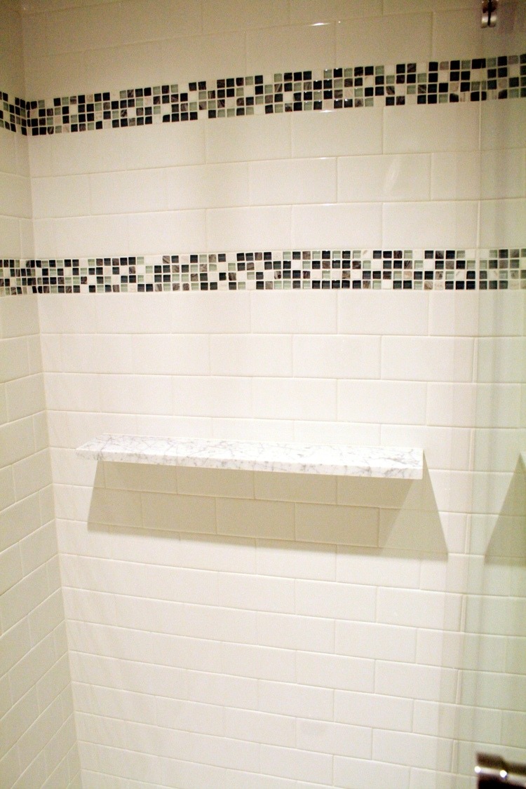 Elegant white-tiled shower with mosaic tile accents and a marble shelf in Maushop remodel