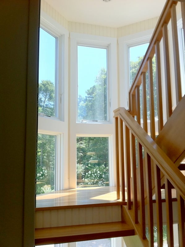 Sunlit staircase with wooden railings in a Cataumet home renovation by At Design Remodel