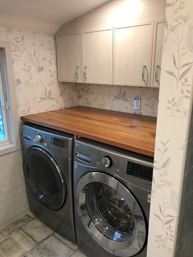 Laundry area with washer, dryer, and wooden countertop in Centerville bathroom remodel by At Design Remodel in Mashpee