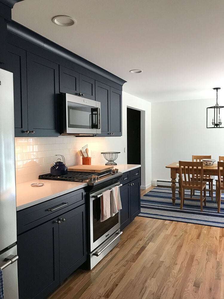 Dining area adjacent to modern kitchen with navy cabinets and wood floors, Dennis Kitchen Remodel by At Design Remodel, Mashpee