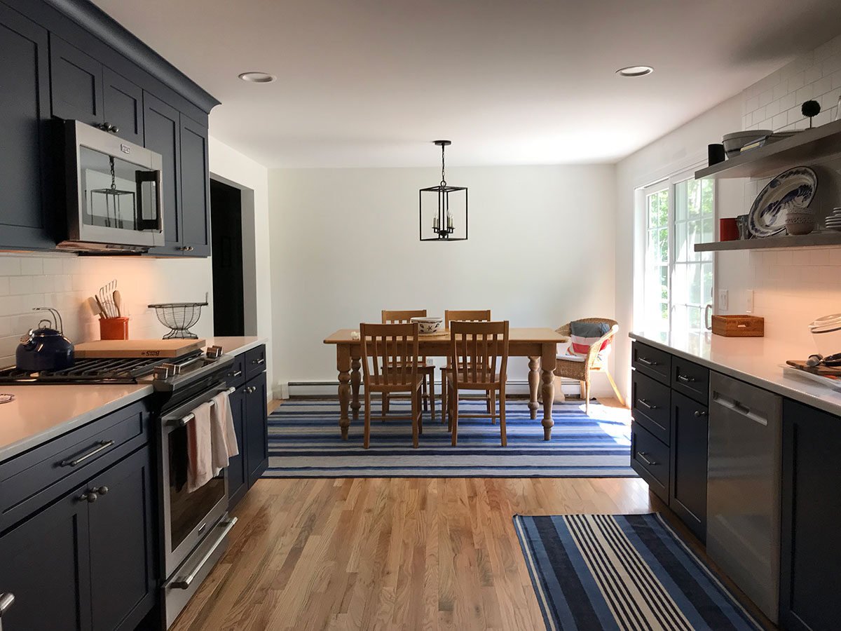 Dining space connected to kitchen with navy cabinets and bright lighting, Dennis Kitchen Remodel by At Design Remodel, Mashpee