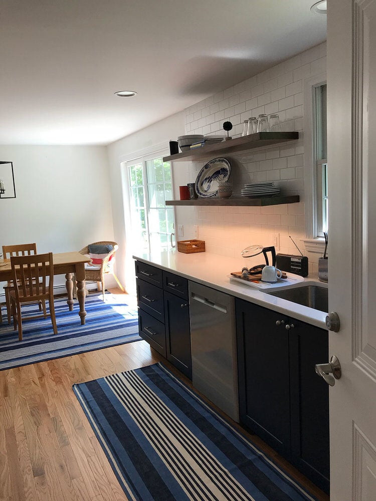 View of renovated kitchen with navy cabinets and a bright dining area, Dennis Kitchen Remodel by At Design Remodel, Mashpee