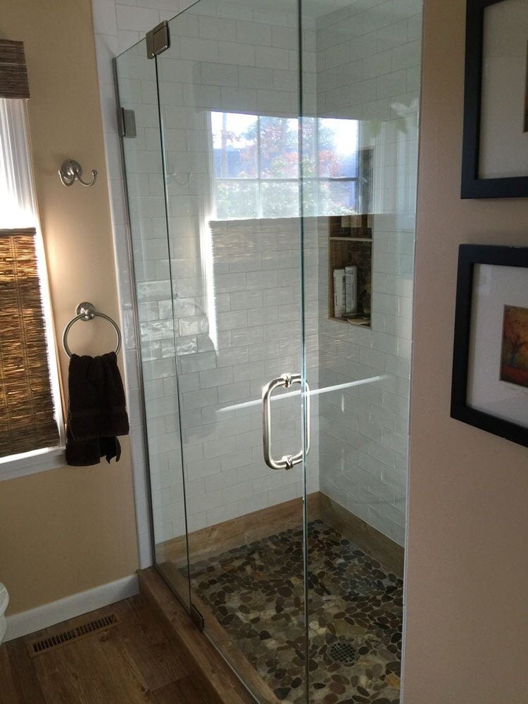 Glass-enclosed shower with pebble tile flooring in a remodeled Falmouth bathroom by At Design Remodel in Mashpee