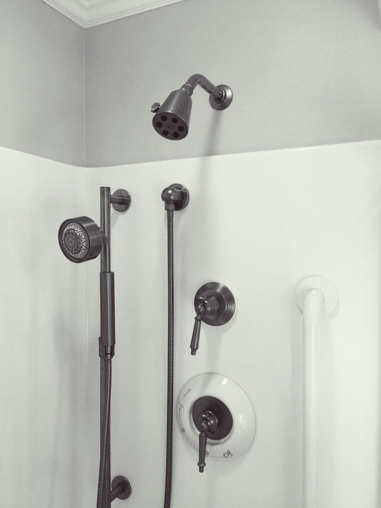 Matte black shower fixtures in a remodeled bathroom with white walls by At Design Remodel in Mashpee