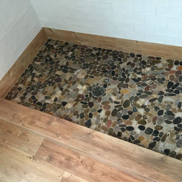 Pebble stone shower floor with natural tones in a custom Falmouth bath renovation by At Design Remodel in Mashpee