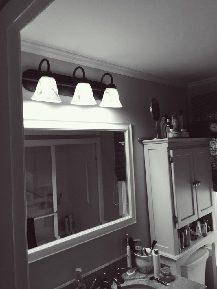 White vanity lighting fixture above the mirror in a home bathroom renovation by At Design Remodel in Mashpee