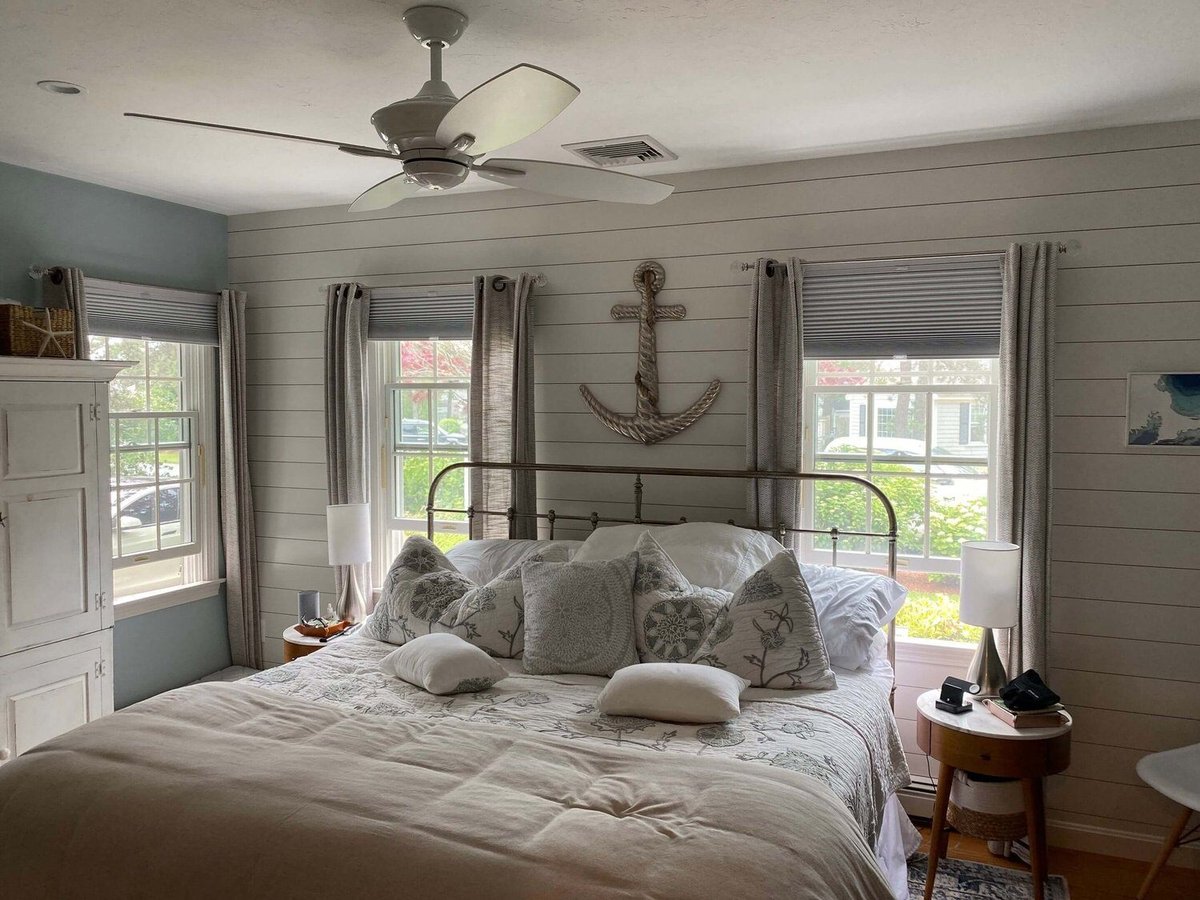 Cozy master bedroom with nautical decor and large windows, custom home remodel by At Design Remodel in Dennis, MA