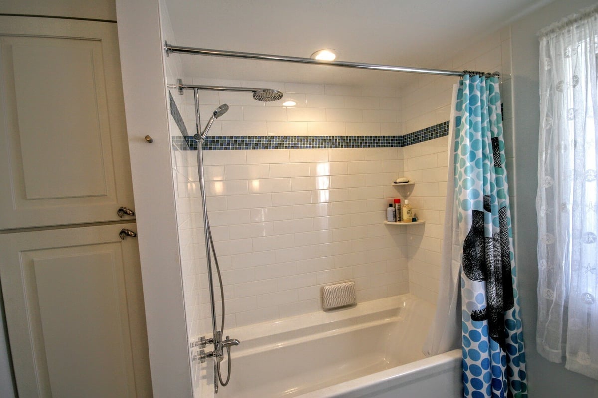 Bathroom remodel featuring a white tiled shower with blue accents by At Design Remodel in Mashpee