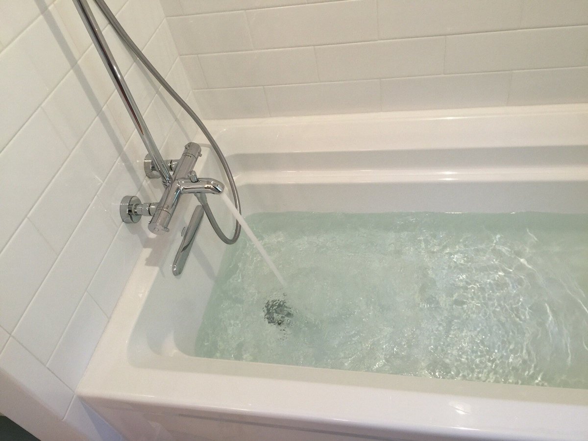 White bathtub with running water in a Mashpee bathroom remodel by At Design Remodel