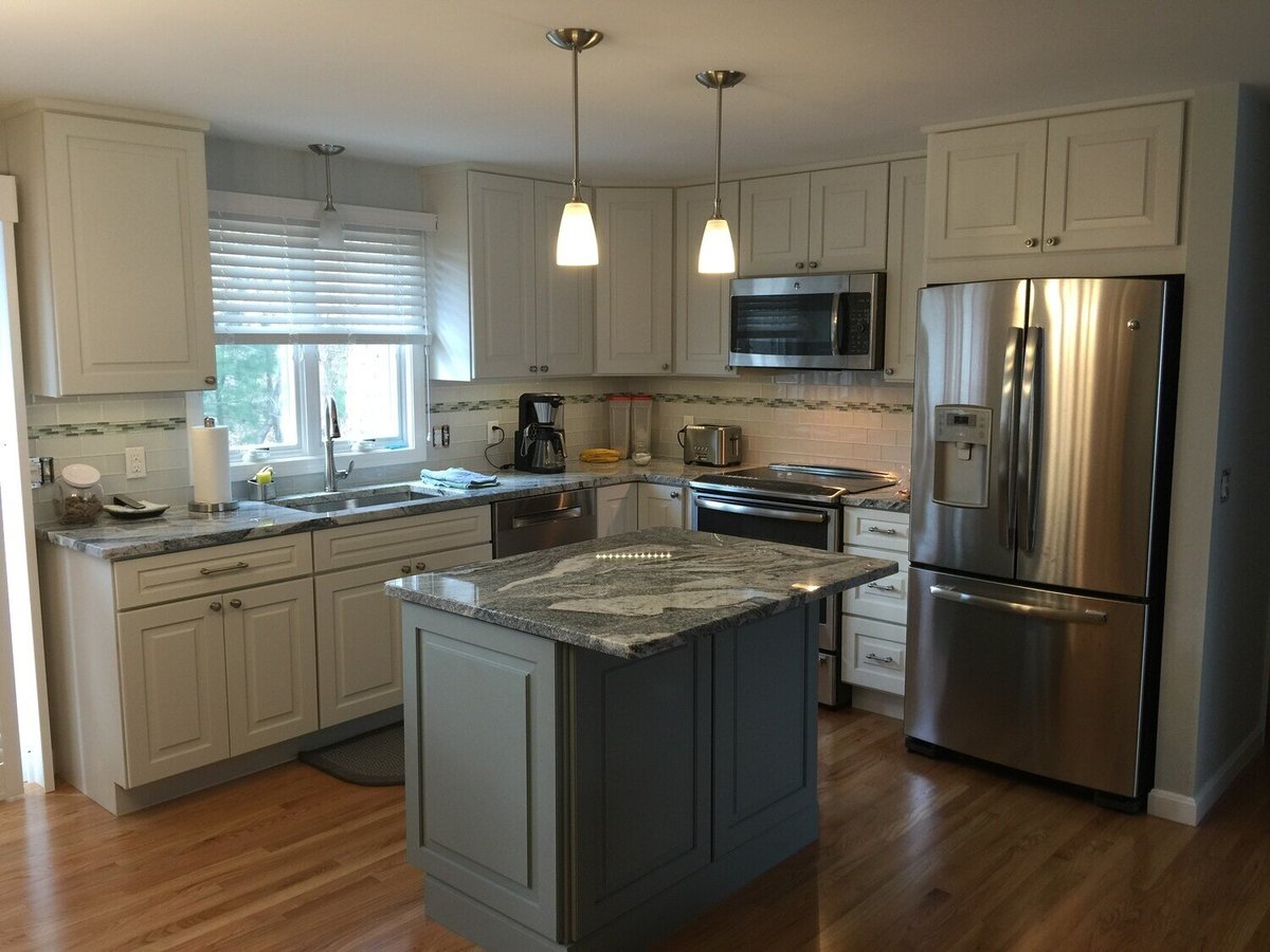 Completed Mashpee kitchen remodel with white cabinets, stainless steel appliances, and an island by At Design Remodel