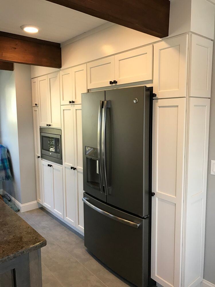 Built-in white cabinetry and stainless steel refrigerator in a remodeled kitchen by At Design Remodel in Mashpee