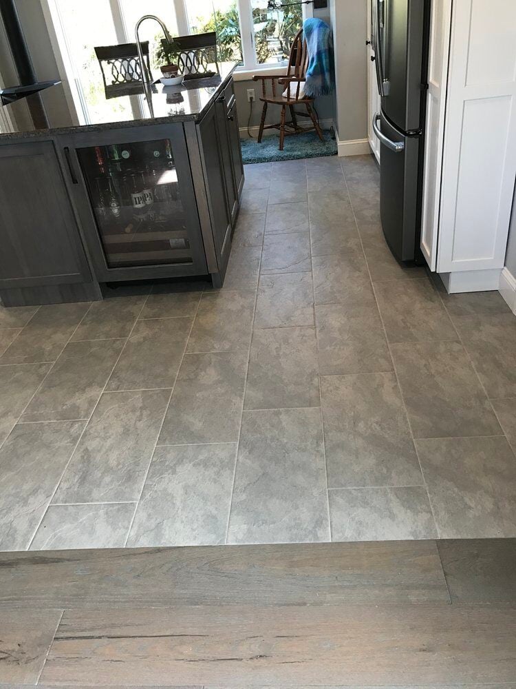 Tile flooring in remodeled kitchen with a large central island by At Design Remodel in Mashpee
