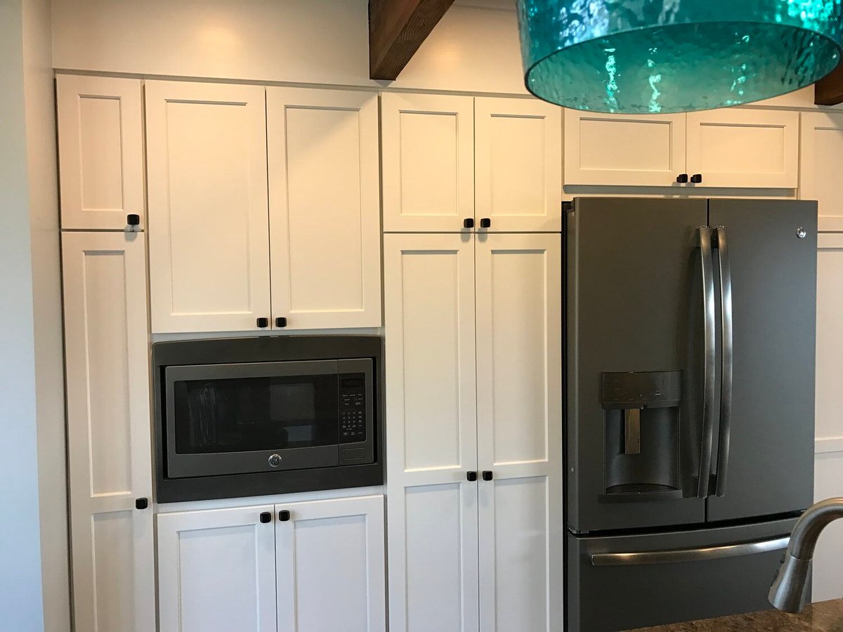 White kitchen cabinets with built-in microwave and refrigerator in Mashpee kitchen remodel by At Design Remodel