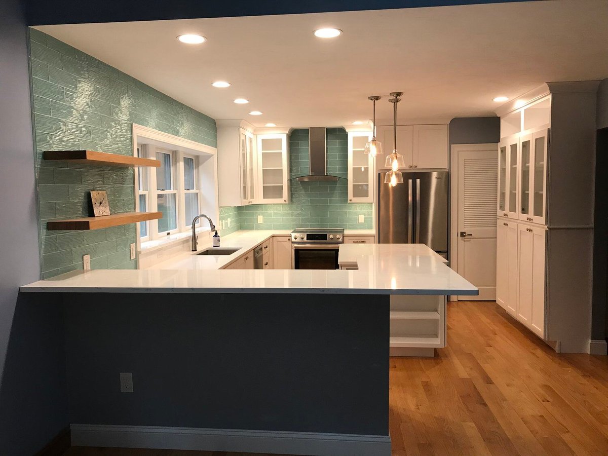 Newly remodeled kitchen in Mashpee with sleek white countertops and teal backsplash by At Design Remodel