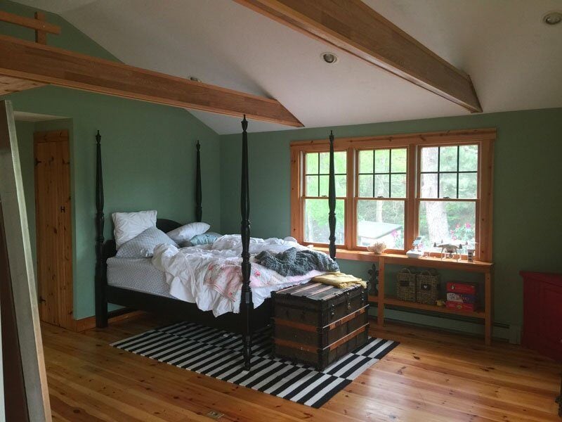 Bedroom with rustic wooden elements and bright window view in a Mashpee lake cottage remodel by At Design Remodel