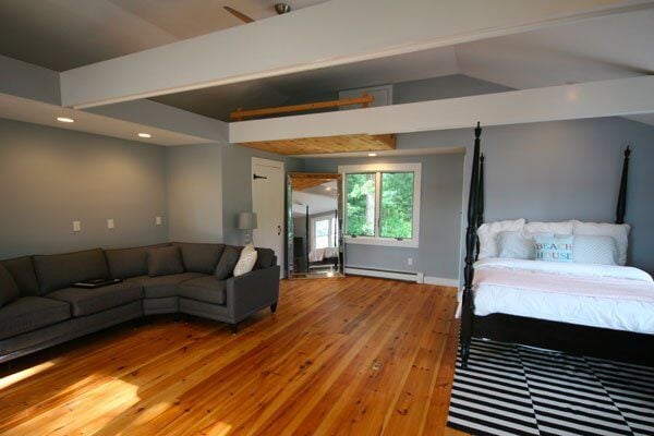Large bedroom with wood floors and four-poster bed in Mashpee cottage renovation by At Design Remodel