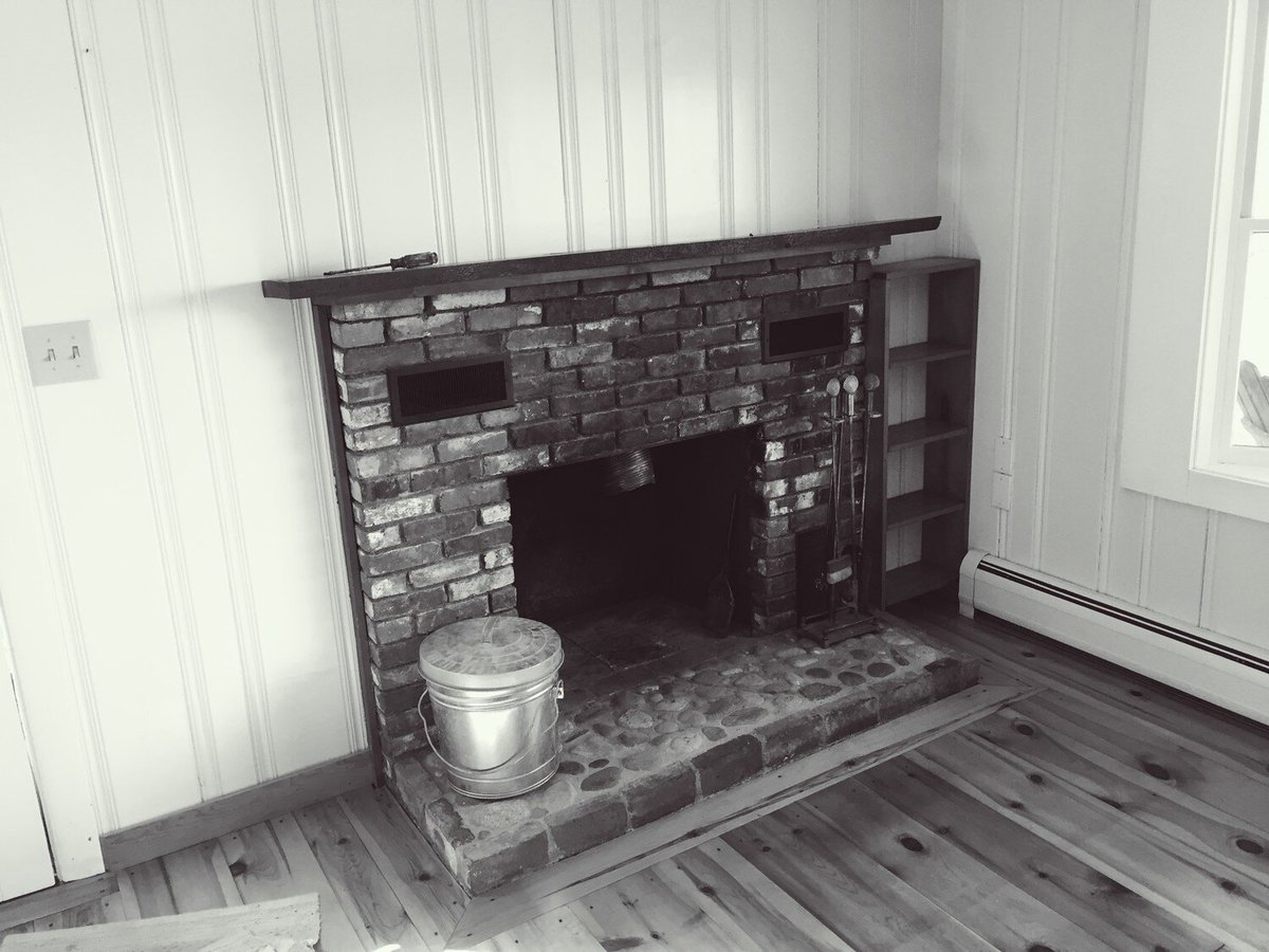 Brick fireplace in a Mashpee Lake Cottage renovation by At Design Remodel, featuring a rustic hearth and wood paneling