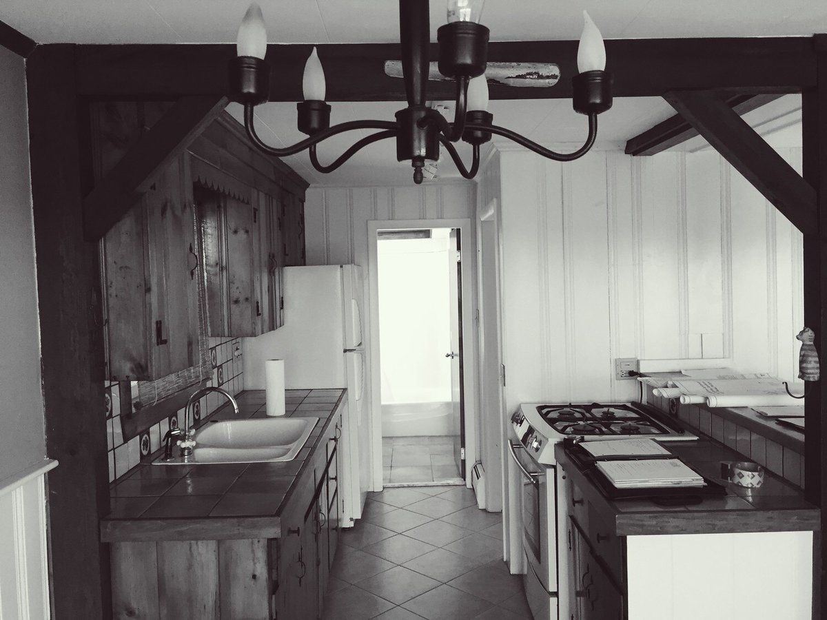 Empty room with wooden beams and light-filled doorway in a Mashpee cottage remodel by At Design Remodel