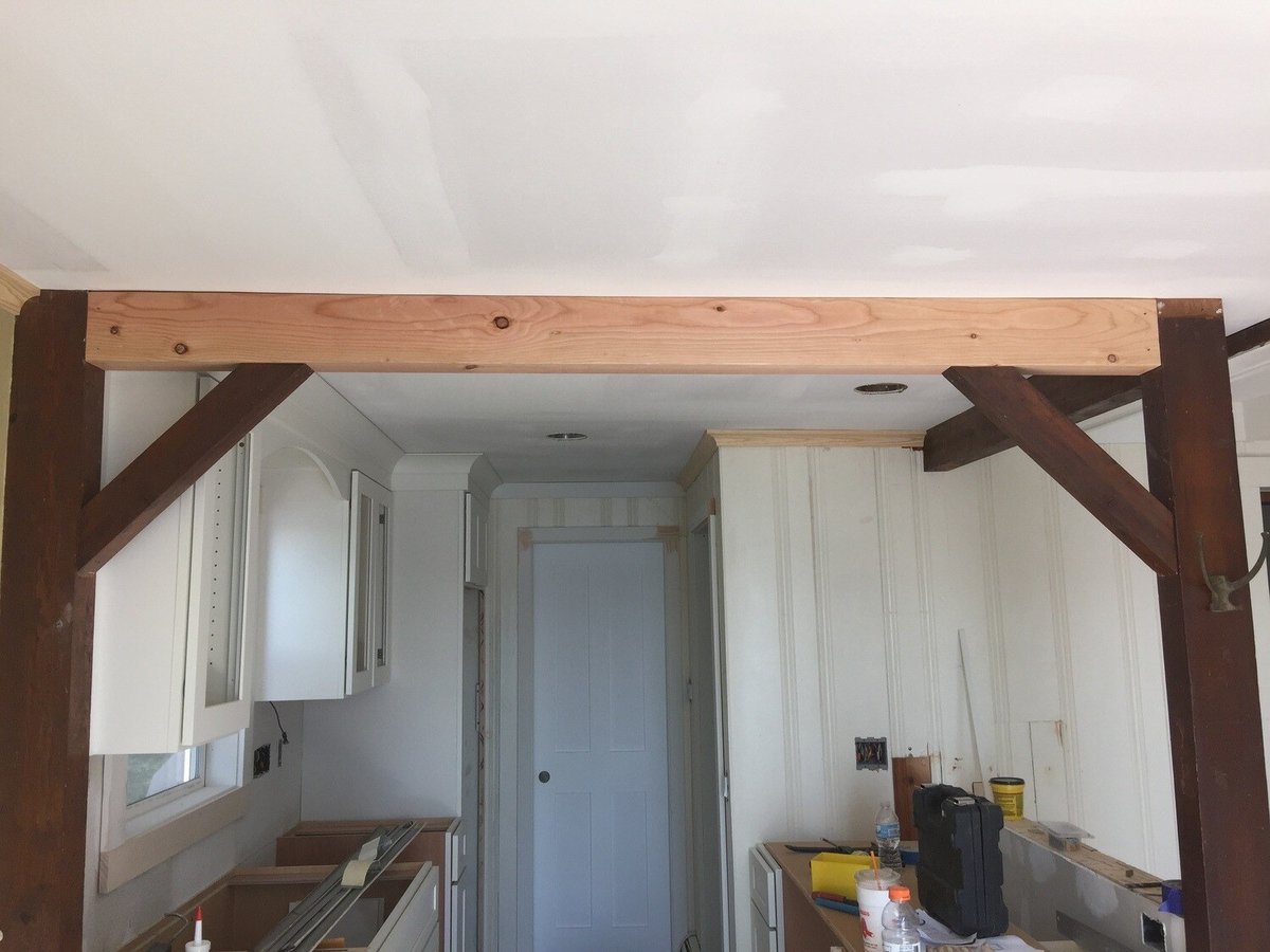 Exposed beams and white cabinets in the kitchen of a lakefront Mashpee cottage renovation by At Design Remodel