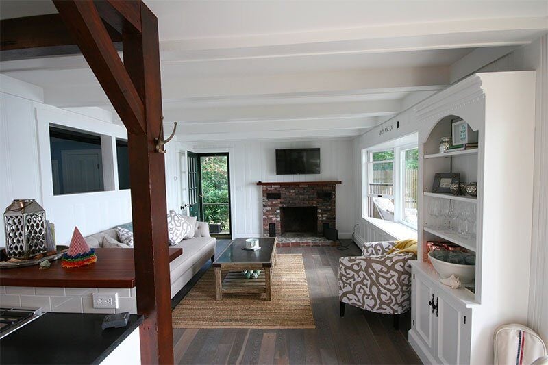 Lakefront living room with brick fireplace and modern decor in Mashpee Lake Cottage, remodeled by At Design Remodel