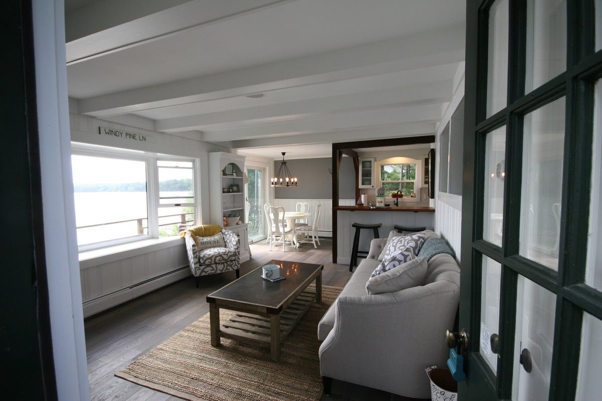 Living room with lake views and modern decor, part of a cottage remodel by At Design Remodel in Mashpee
