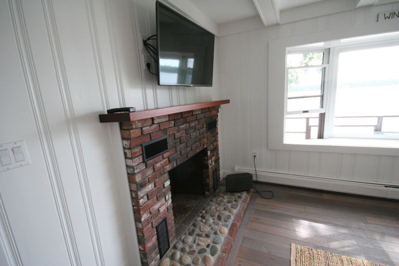 Restored brick fireplace with TV in a Mashpee lakefront cottage, part of a remodel by At Design Remodel