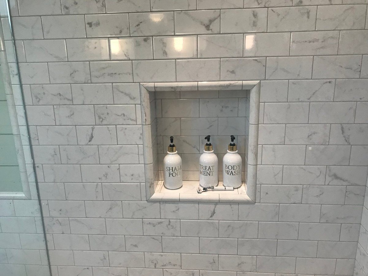 Built-in niche with shampoo bottles set in a marble shower in New Seabury bathroom remodel