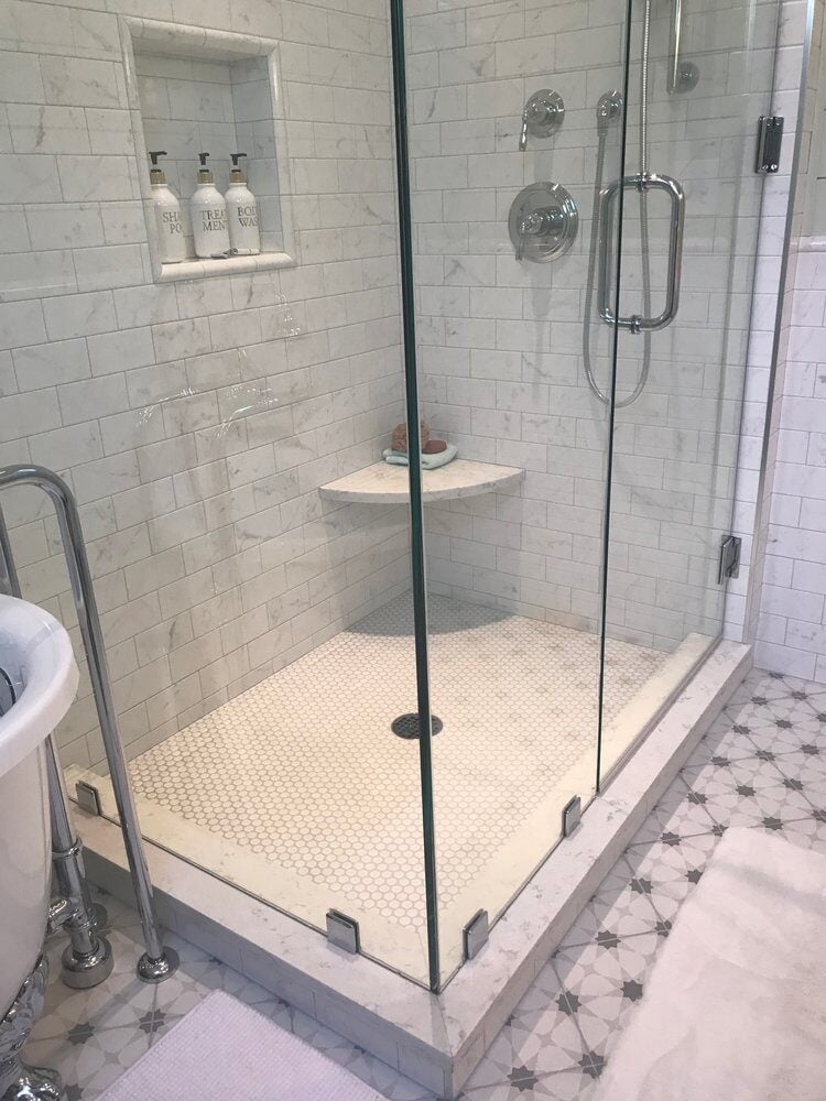 Elegant white-tiled shower with glass doors and marble accents in New Seabury bathroom remodel