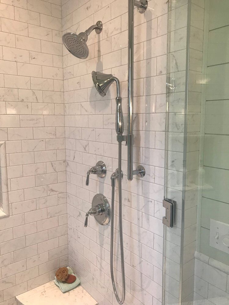 Polished chrome shower fixtures against white marble tiles in New Seabury bathroom remodel