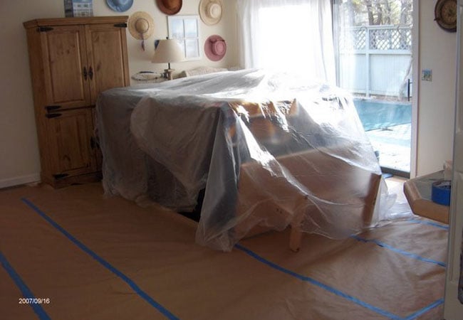 Furniture covered with plastic in living room during New Seabury remodel by At Design Remodel, Mashpee