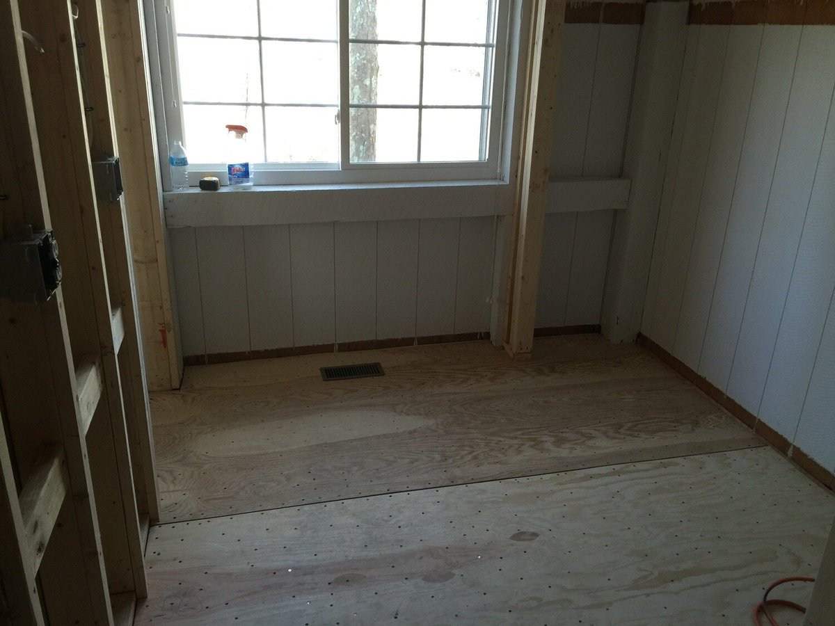 Bathroom in New Seabury under construction, showcasing plywood floors and framing by At Design Remodel