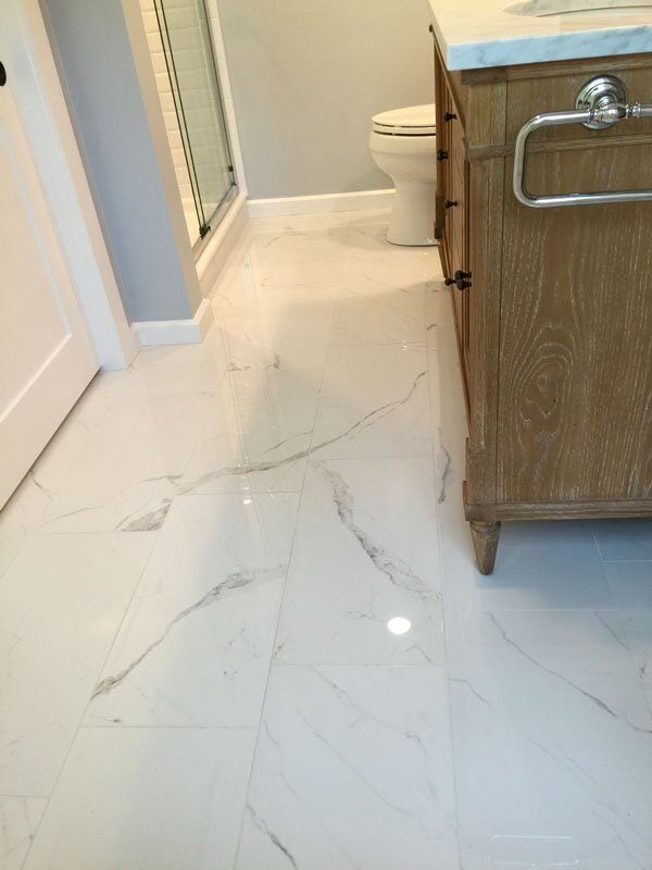 Marble tiled bathroom floor with wooden vanity, part of a Mashpee remodel by At Design Remodel