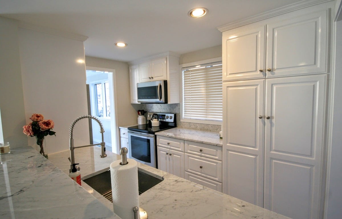 Contemporary kitchen featuring marble countertops and white cabinetry, part of New Seabury Mews condo remodel by At Design Remodel