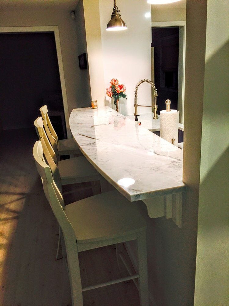 Nighttime view of kitchen island with marble countertops in New Seabury Mews condo, remodeled by At Design Remodel