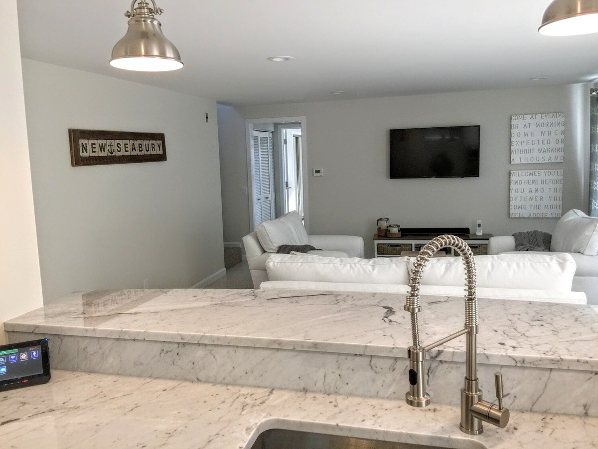 Open kitchen with marble countertop and white cabinetry in New Seabury Mews condo, remodeled by At Design Remodel