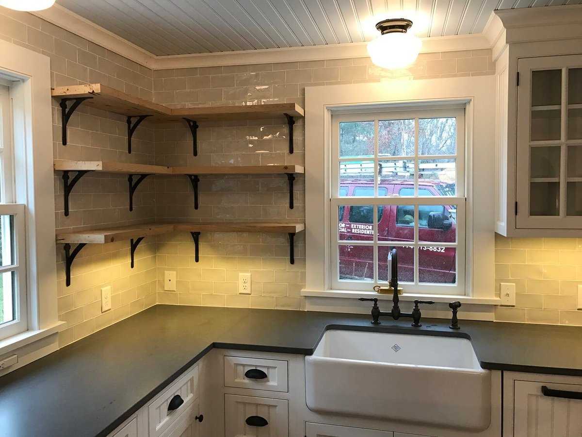 White farmhouse sink and floating wood shelves in a Falmouth kitchen remodel by At Design Remodel