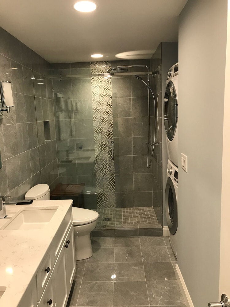 Full bathroom view with walk-in shower and laundry units in a Yarmouthport remodel by At Design Remodel