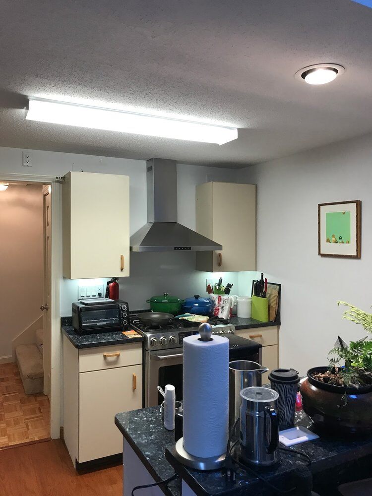 Small kitchen setup before renovation with white cabinets and hood vent in Yarmouthport by At Design Remodel, Mashpee